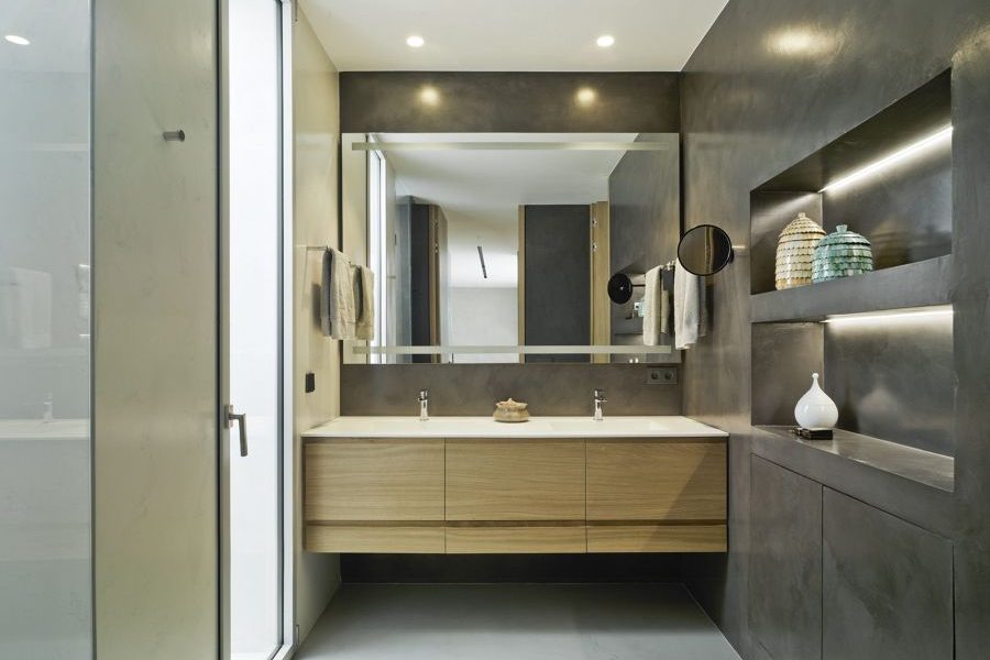 Bathroom with dark grey microcement walls, a wooden vanity and an illuminated mirror