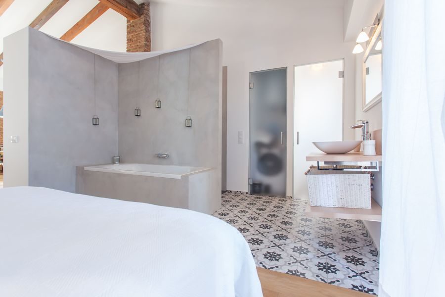 Bathtub and light grey microcement partition beside a patterned cement tile floor